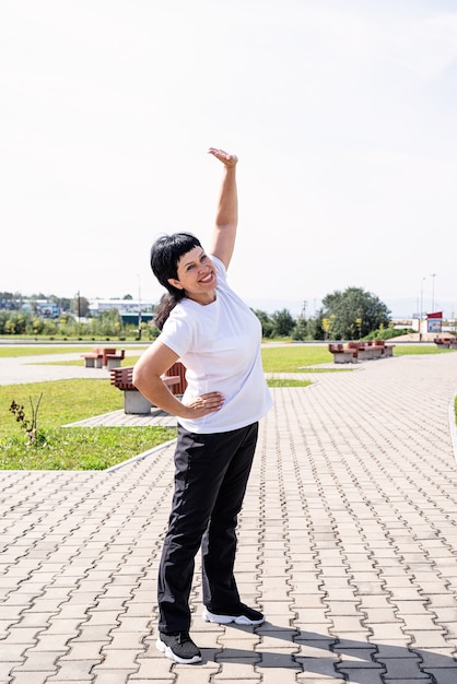 Mulher sênior sorridente se aquecendo, alongando-se ao ar livre no parque