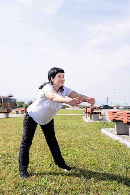 Mulher sênior sorridente se aquecendo, alongando-se ao ar livre no parque