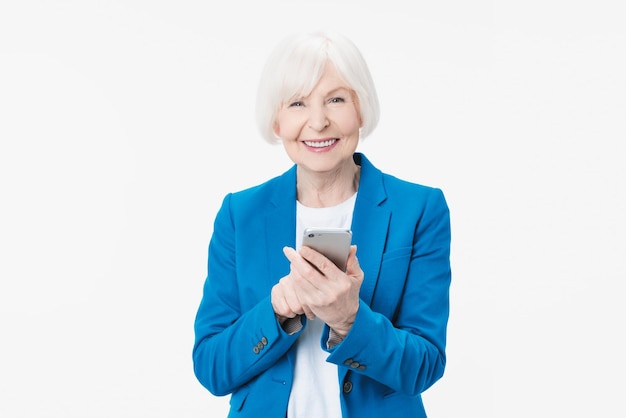 Mulher sênior sorridente segurando smartphone usando aplicativos móveis online sobre fundo branco