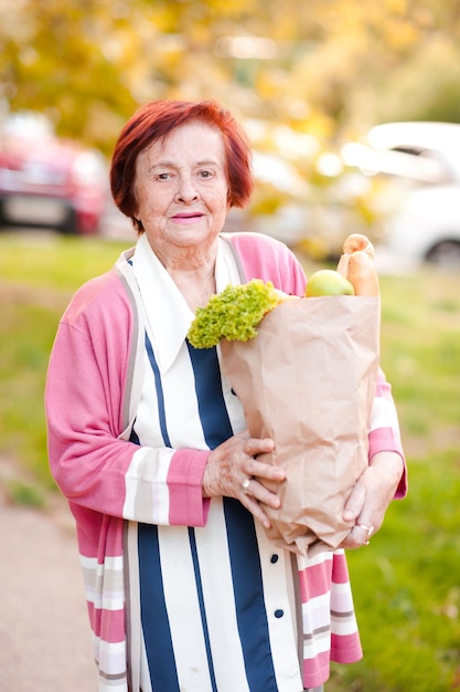 Mulher sênior sorridente segurando um saco de papel com produtos ao ar livre