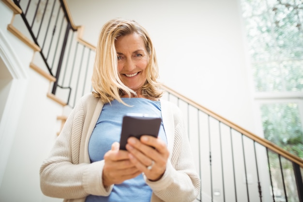 Mulher senior sorridente, usando o celular em casa