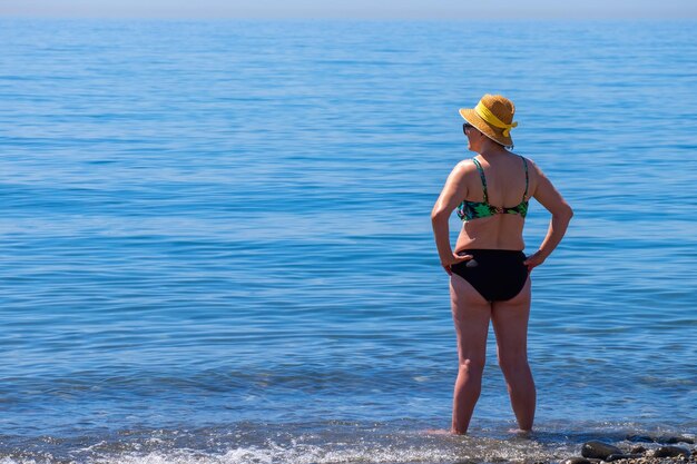 Mulher sênior sozinha em frente ao mar mediterrâneo em uma praia em um dia ensolarado de verão