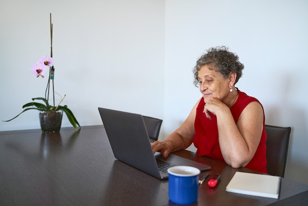 Mulher sênior usando computador para navegar na Internet de casa