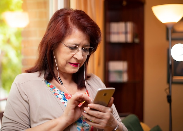 Mulher sênior, usando, nova tecnologia, chamadas, com, dela, telefone celular, e, fones