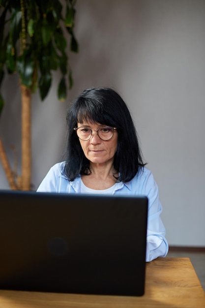 Mulher sênior usando óculos digitando no laptop, mensagens, bate-papo