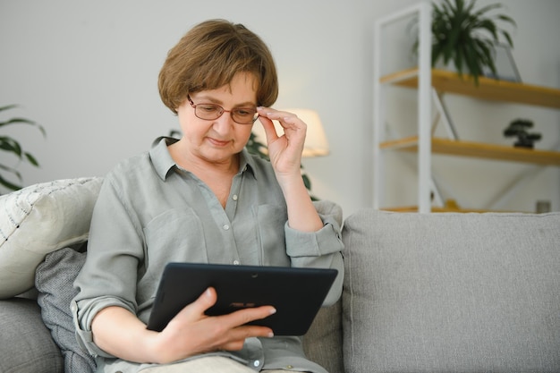 Mulher sênior usando tablet digital na sala de estar em casa