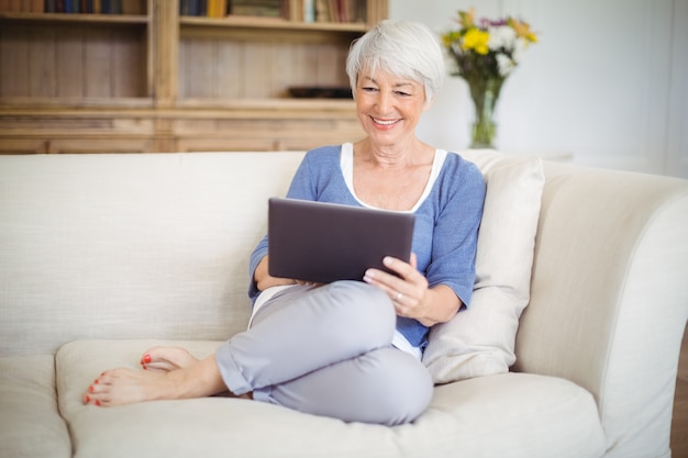 Mulher sênior usando tablet digital na sala de estar