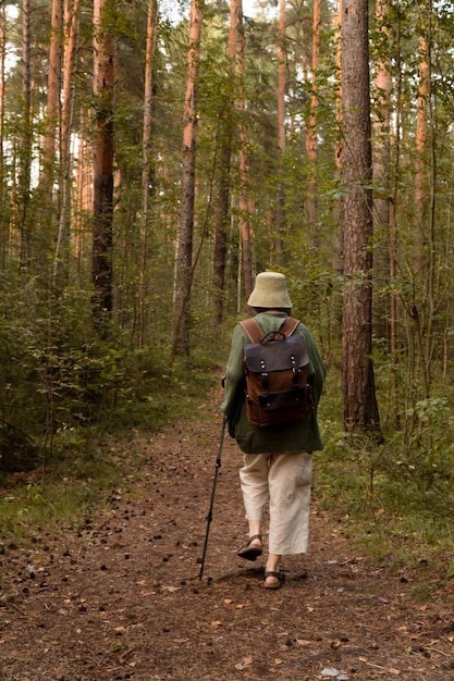 Mulher sênior viajante com mochila em caminhada na floresta verde