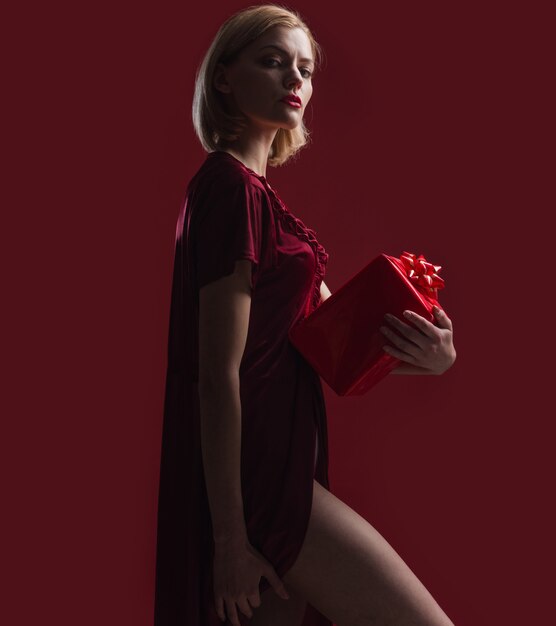 Mulher sensual com caixa de presente. Menina de vestido vermelho com presente.