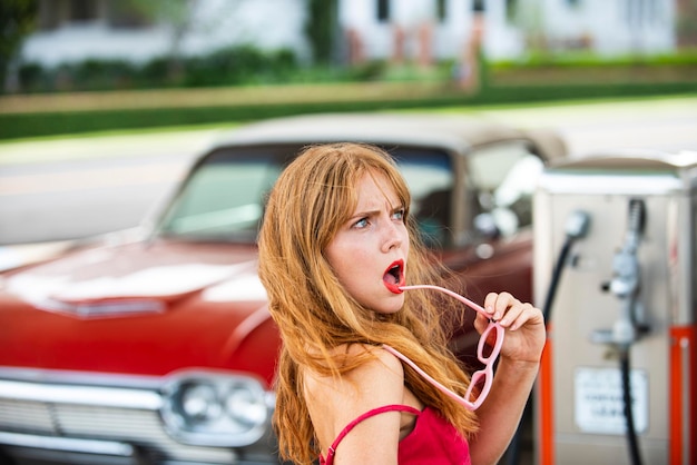 Mulher sensual em posto de gasolina contra automóvel retro vermelho