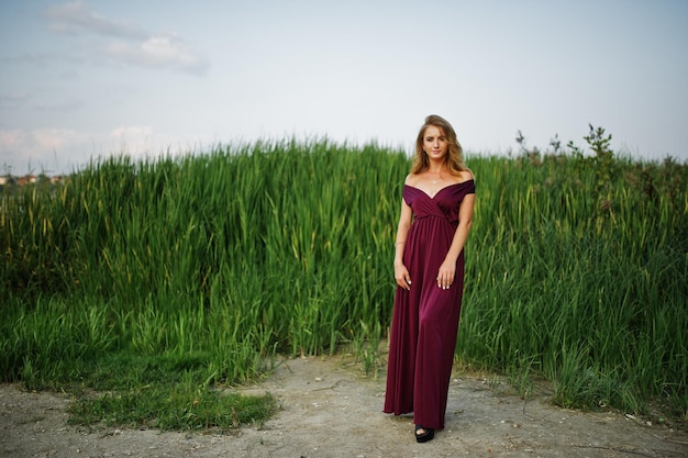 Mulher sensual loira de vestido vermelho marsala posando nos juncos