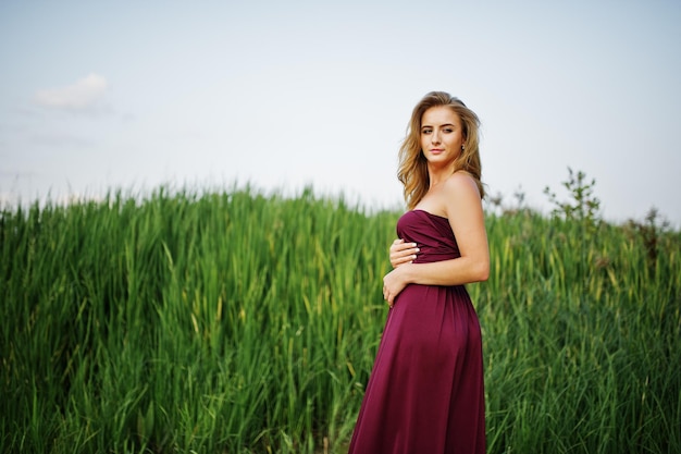 Mulher sensual loira de vestido vermelho marsala posando nos juncos