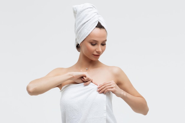 Mulher sensual na toalha branca fofa na cabeça olhando para o dedo tocando a toalha no corpo
