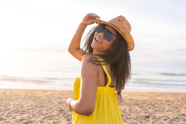 Mulher sensual usando óculos escuros e chapéu de sol posando sorrindo para a câmera na praia