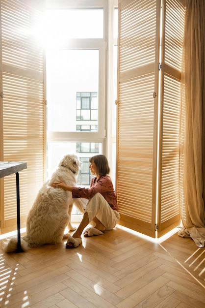 Mulher senta-se com cachorro pelas cortinas da janela em casa