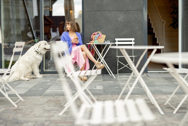 Mulher senta-se com seu adorável cachorro branco no café em uma rua