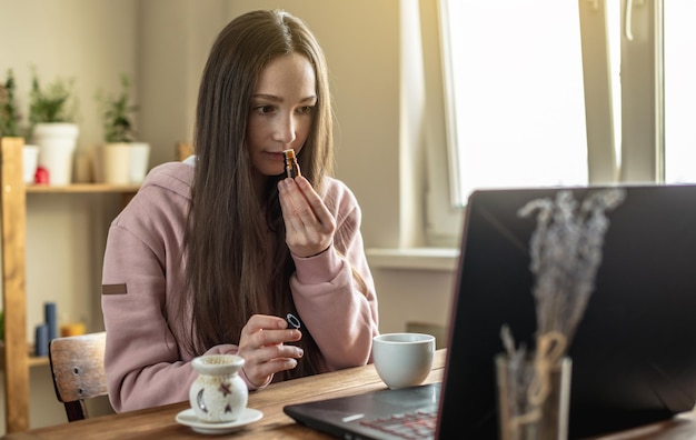 Mulher senta-se em frente a uma tela de computador e cheira óleo essencial de uma garrafa para relaxar e restaurar energia ou para ensino à distância sobre óleos e sessão de meditação