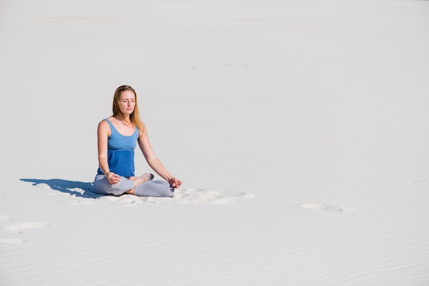Mulher senta-se na areia em posição de lótus yoga