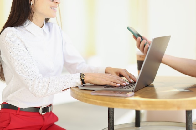 Mulher sentada à mesa no bar com um amigo e digitando no close do teclado do laptop. Conceito de site de reuniões