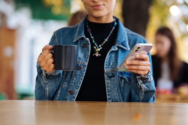 Foto mulher sentada ao ar livre café bebendo bebida segurando na mão smartphone