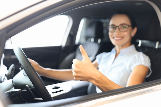 Mulher sentada ao volante de um carro e mostrando o polegar para cima, close up, comprando carro no conceito de crédito