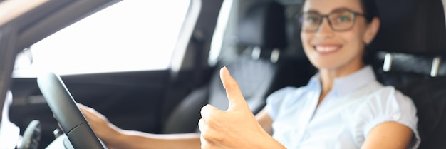 Mulher sentada ao volante de um carro e mostrando o polegar para cima, close-up, comprando carro no conceito de crédito