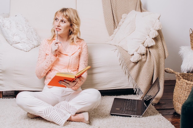 Mulher sentada com livro e laptop no chão