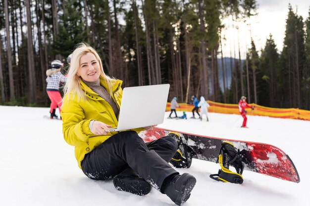 mulher sentada com um laptop em uma montanha de inverno em uma paisagem de fundo