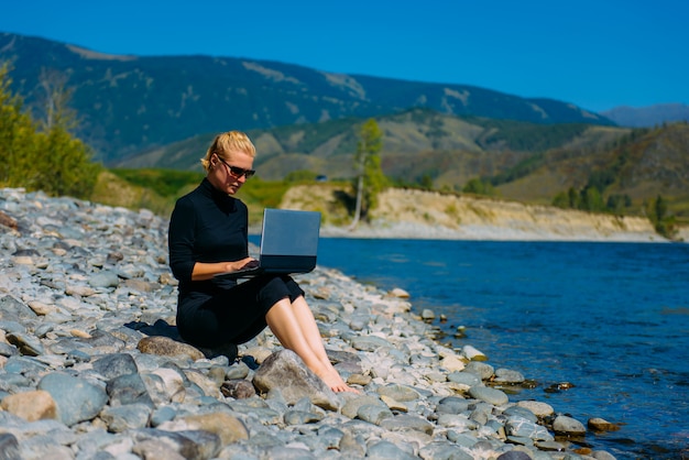 Mulher sentada com um laptop perto de um rio