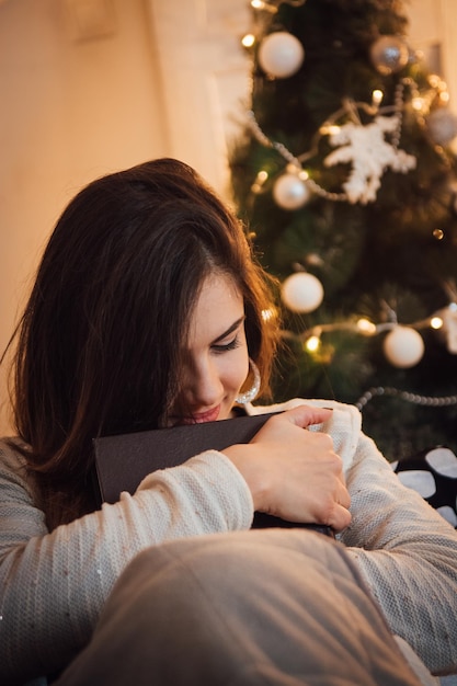 Mulher sentada contra a árvore de Natal em casa