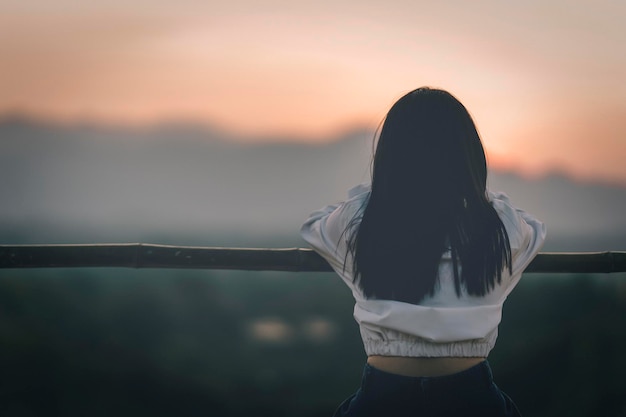 Mulher sentada de costas olhando o pôr do sol