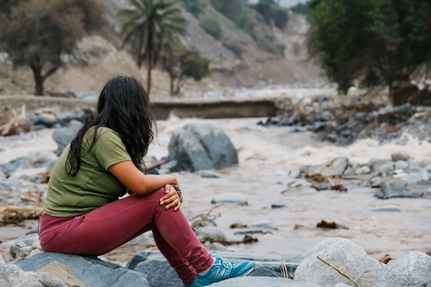 Mulher sentada de costas para a margem de um rio poderoso