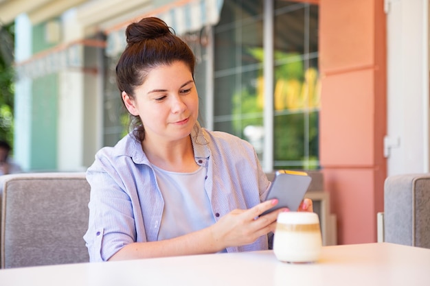 Mulher sentada do lado de fora e fazendo fotografia de seu café com caneca