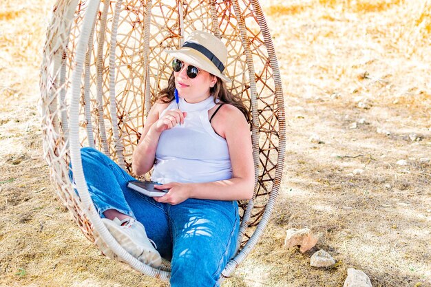 Mulher sentada em cadeira de ovo de vime pendurada relaxante verão