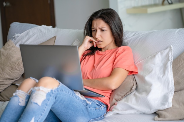 Mulher sentada em casa no sofá com um laptop