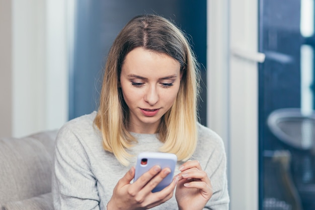 mulher sentada em casa no sofá e usando um telefone celular descansando do trabalho