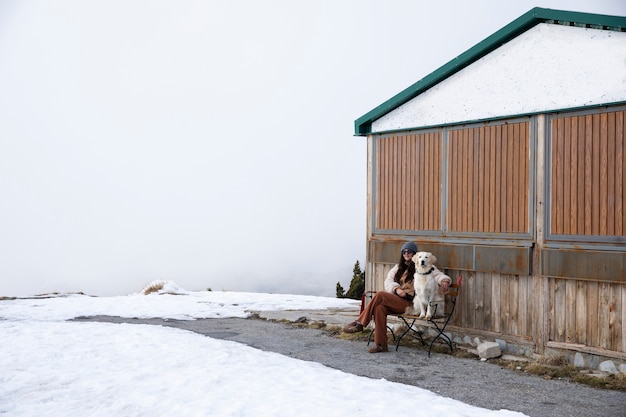 Foto mulher sentada em um banco com seu labrador durante a viagem de inverno