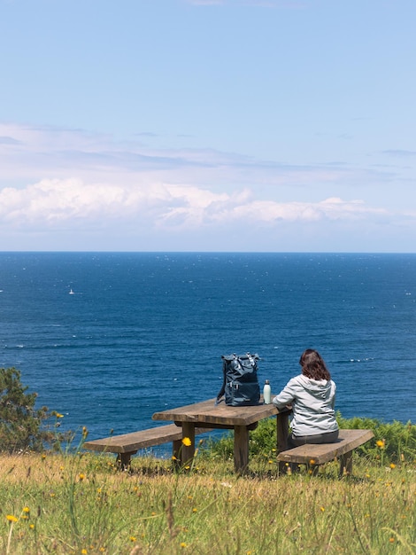 Foto mulher sentada em um banco de madeira de costas contemplando a vista para o mar