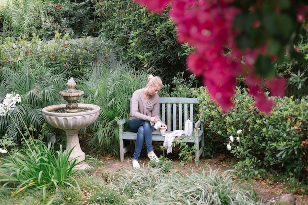 Mulher sentada em um banco de madeira em um jardim fazendo uma pausa