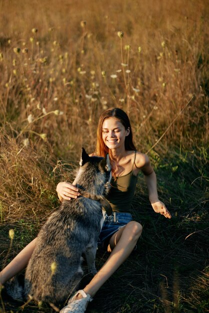 Mulher sentada em um campo com um cachorro bassê sorrindo enquanto passa o tempo na natureza com um cachorro amigo no outono ao pôr do sol