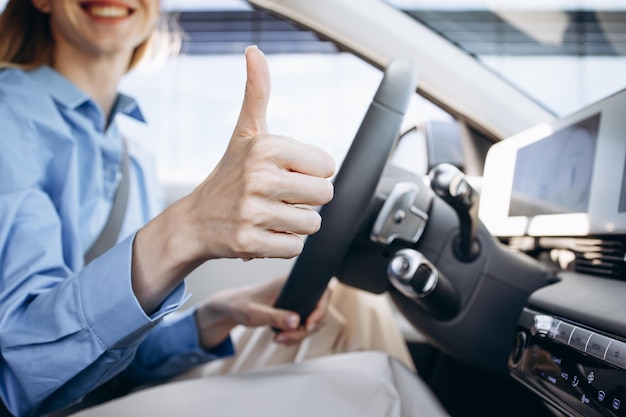 Foto mulher sentada em um carro elétrico e mostrando o dedo polegar para cima