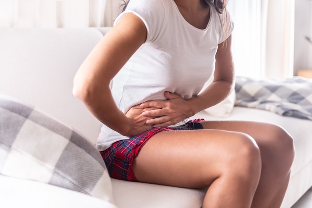 Mulher sentada em um sofá em casa, segurando o apêndice, com dor de estômago.