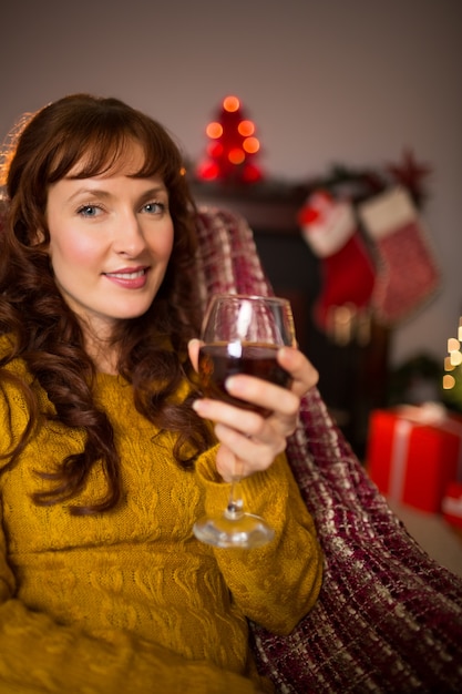 Mulher sentada em um sofá segurando um copo de vinho tinto