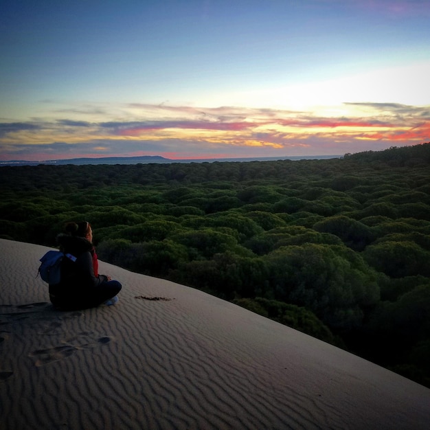 Foto mulher sentada em uma paisagem contra o céu durante o pôr do sol