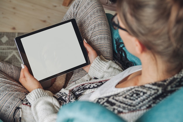 Mulher sentada em uma poltrona aconchegante, com cobertor quente, usando tablet