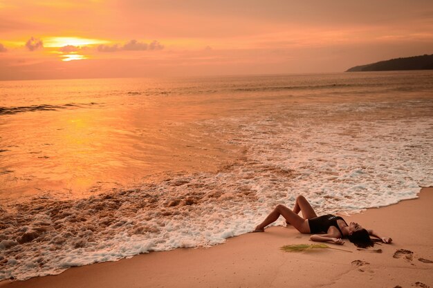 Mulher sentada na areia da praia com ondas tocando seus pés