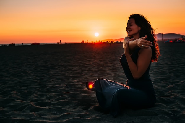 Mulher sentada na areia da praia e relaxar ao pôr do sol