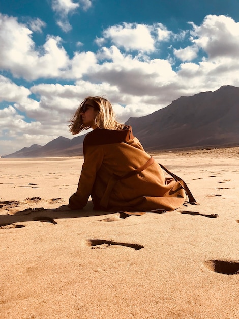 Foto mulher sentada na areia na praia contra o céu nublado