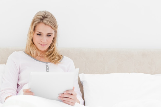 Mulher sentada na cama, segurando e assistindo um tablet PC