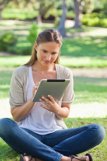 Mulher sentada na grama enquanto usa seu tablet computador